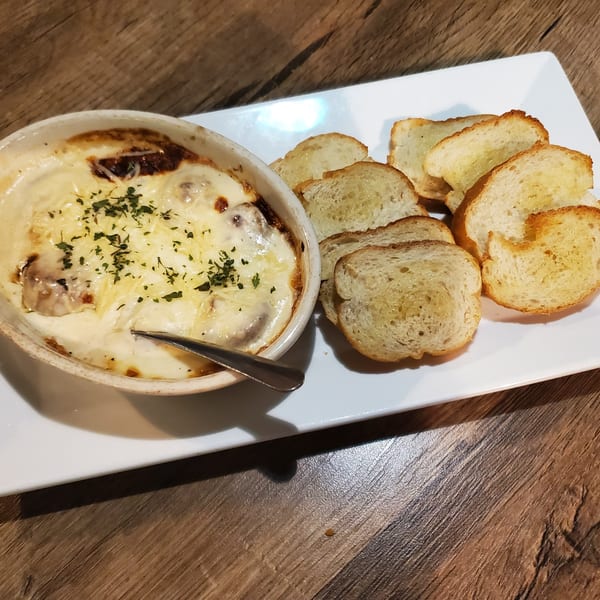 Creamy mushroom gratin with melted cheese and herbs, served with toasted bread slices on a white plate.