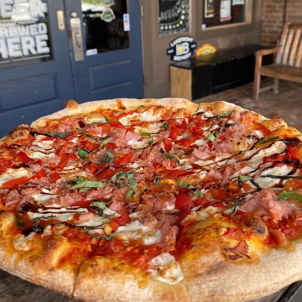 The Mill House pizza, topped with ham, red peppers, basil, and a balsamic glaze, outdoors.