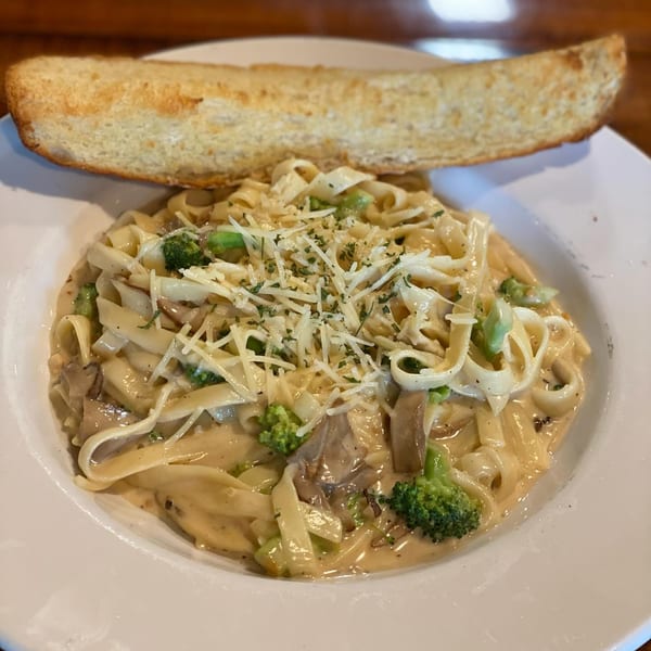 Creamy pasta with broccoli, mushrooms, and shredded cheese, served with a side of garlic bread.