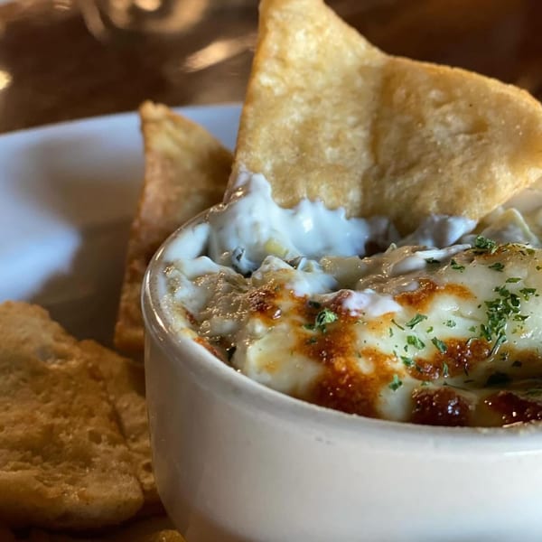 A close-up of a creamy dip with melted cheese and herbs, served with crispy tortilla chips.