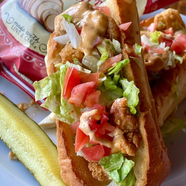 Two fried shrimp po'boy sandwiches with lettuce, tomato, and sauce, served with a pickle spear.