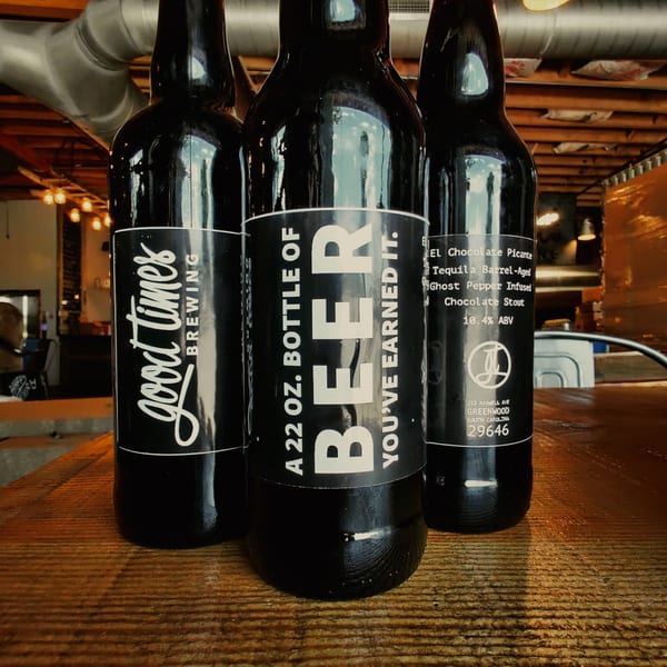 Three dark beer bottles with black and white labels on a wooden table at The Mill House.