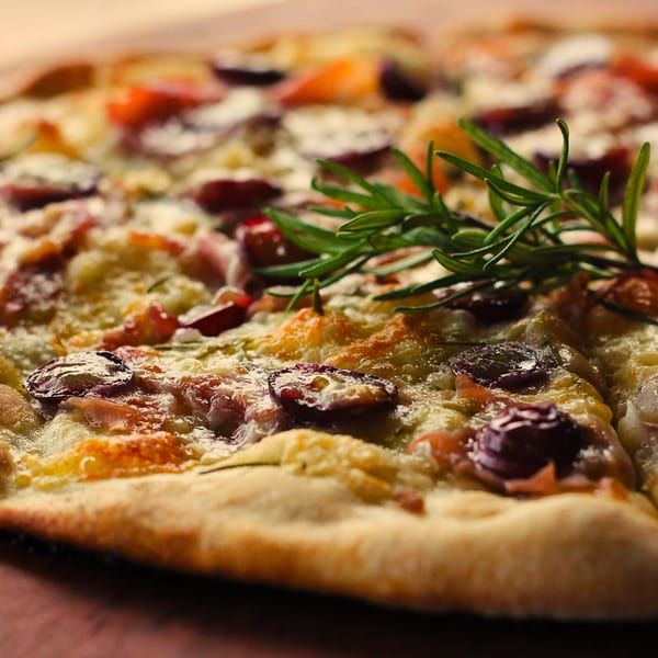 Close-up of a Mill House pizza with melted cheese, olives, and rosemary garnish.