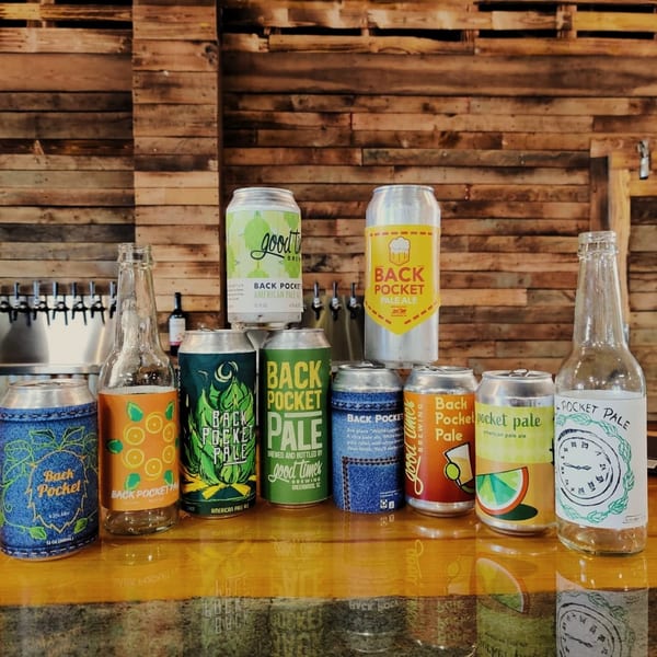 Assortment of Back Pocket Pale Ale cans and bottles on a wooden counter with beer taps in the background.
