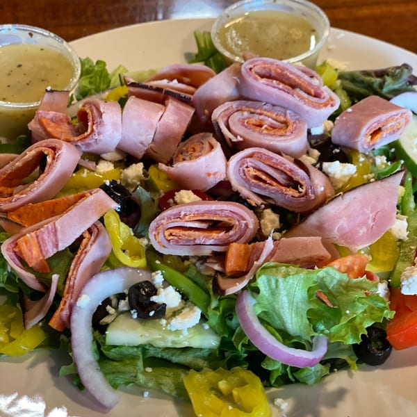 A close-up of a vibrant Italian salad with rolled meats, olives, peppers, and feta cheese.