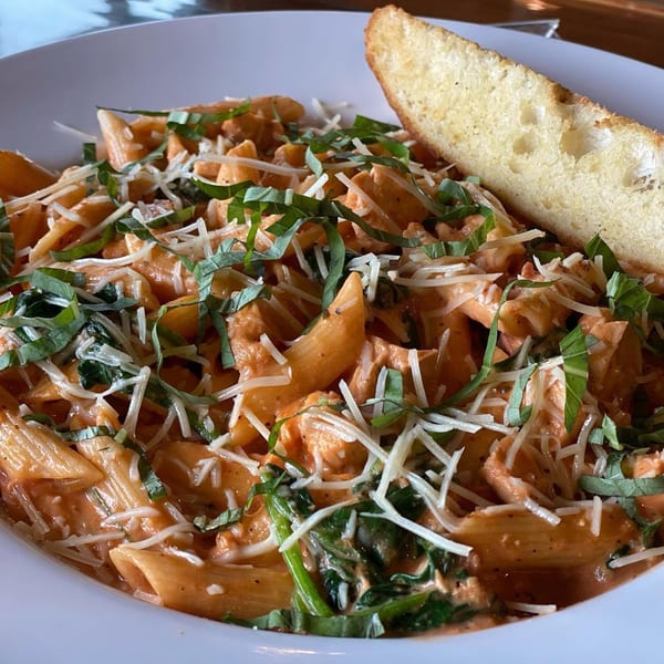 Penne pasta with creamy tomato sauce, spinach, shredded cheese, basil, and a side of garlic bread.