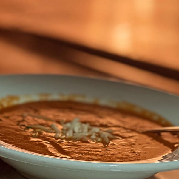 A bowl of creamy tomato soup topped with shredded cheese and a spoon, at The Mill House.