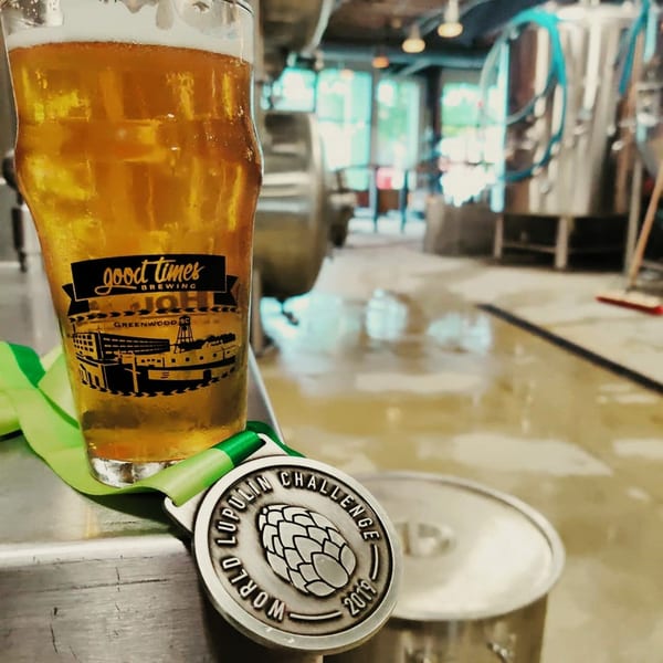 A glass of beer with a brewery logo and a "World Lupulin Challenge 2019" medal.